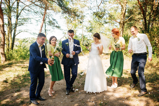 Wedding couple with bridesmaids and best drinking champagne at sunny wood.