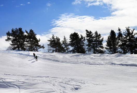 Two hikers on snow slope in sun winter day