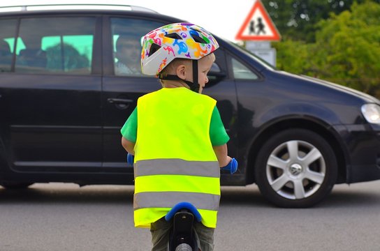 Little boy riding a bike and wearing reflective vest and helmet on the road. Driving car in front of him.