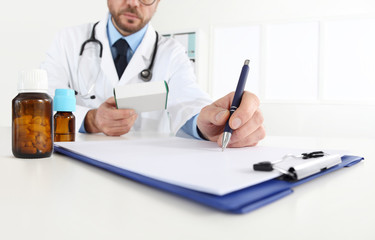 doctor writing RX prescription in medical office with drugs on desk