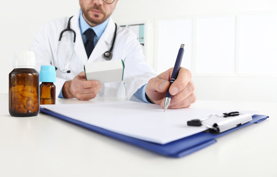 doctor writing RX prescription in medical office with drugs on desk