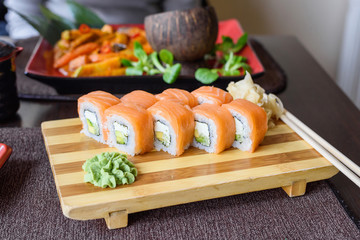 Philadelphia salmon sushi rolls on a wooden plate in a traditional japanese restaurant, ginger, wasabi, shrimp, avocado, cream cheese, cucumber and tobiko caviar