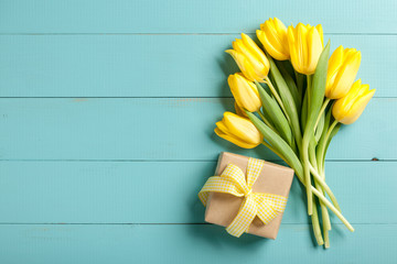 Yellow tulips and gift box on blue wooden background