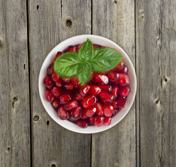 Pomegranate seeds on wooden background. Red grains of a pomegranate in ceramic bowl. Sweet and juicy garnet with copy space for text. Top view.