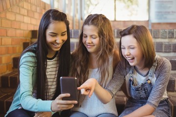 Smiling schoolgirls sitting on the staircase using mobile phone 