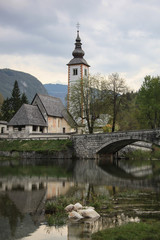 Fototapeta na wymiar Old stone bridge leads to historical church beside the Lake Bohinj, Slovenia