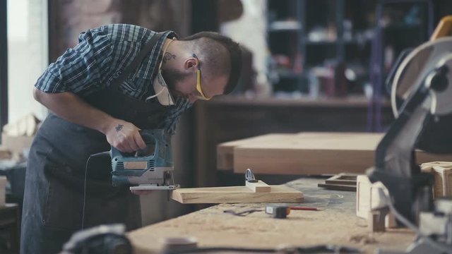Image of carpenter in the workshop. Carpenter cutting wooden board at his workshop. Workplace of cabinetmaker. Carpenter works with a planer in a workshop for the production of vintage furniture.