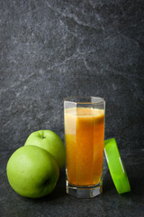 fitness bracelet glass with natural juice and apples on a stone against a dark background