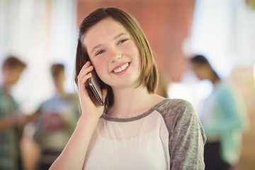 Smiling schoolgirl talking on mobile phone in corridor