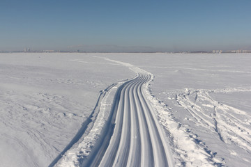 Fototapeta na wymiar Trace of a snowmobile and sled on a snowy surface of frozen reservoir, Siberia, Ob River