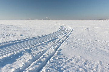 Fototapeta na wymiar Trace of a snowmobile and sled on a snowy surface of frozen reservoir, Siberia, Ob River