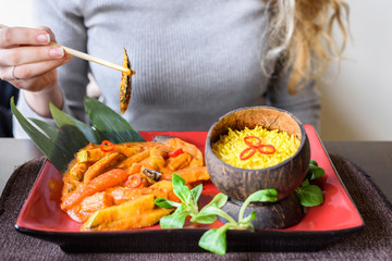 Woman with blonde hair eating with chopsticks traditional vegetable mix with curry sauce and rice...