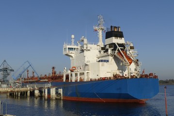 Fototapeta premium Products Tanker discharging at the Oil Terminal with blue hull and red main deck on a sunny day.