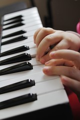 Obraz premium Small kid hands playing notes on MIDI keyboard with miniature keys