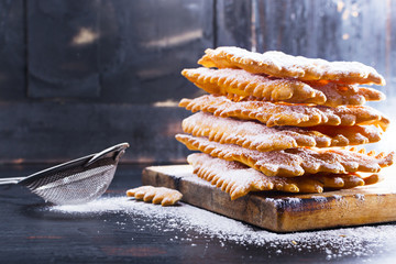 Frappe   - typical Italian carnival fritters dusted with powdered sugar on   old black wooden...