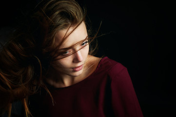 Beautiful girl looking to the side, in profile, Hair flying. Drama. Studio photography in low key on a background