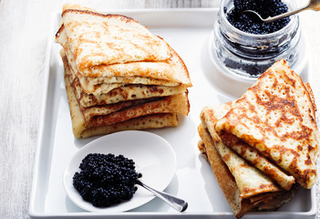 Stack of pancakes with black caviar on a white plate. Selective focus.