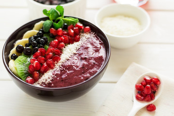 Healthy breakfast: fresh smoothie with kiwi, banana, garnet seeds, blueberry and coconut decorated mint leaves on white wooden table. Selective focus