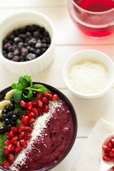 Healthy breakfast: fresh smoothie with kiwi, banana, garnet seeds, blueberry and coconut decorated mint leaves on white wooden table. Selective focus