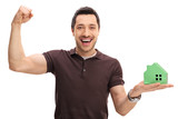 Cheerful guy holding a model house and gesturing happiness