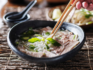 eating bowl of beef brisket pho with chopsticks and spoon
