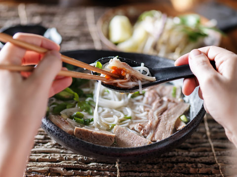 woman eating pho with sriracha using chopsticks and spoon together