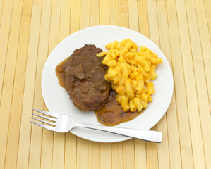 Salisbury steak meal on a plate with a fork atop a wood place mat.