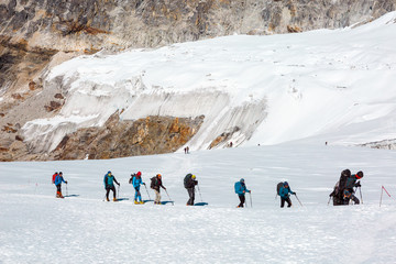 Mountain Climbers walking on snowy Glacier among high Peaks