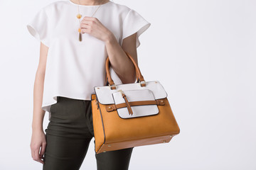 Stylish woman in modern clothes with bright orange white handbag in hands posing at studio isolated...