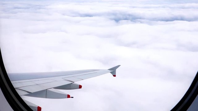 Blick aus einem Flugzeugfenster &uuml;ber den Wolken