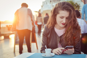 Attractive woman using smart mobile phone in cafe or restaurant, sunny background outdoors