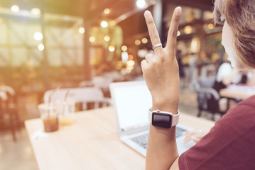 Hands of woman wearing smartwatch and thinking about her work. Female working on laptop in a cafe.