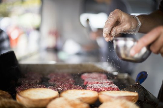 Meat patties being seasoned with salt