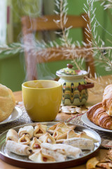 Black tea in yellow mug with croissants, buns and homemade cookies on wooden table