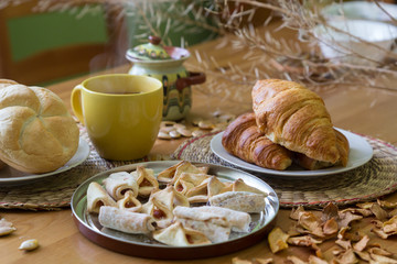 Black tea in yellow mug with croissants, buns and homemade cookies on wooden table