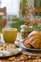 Black tea in yellow mug with croissants, buns and homemade cookies on wooden table