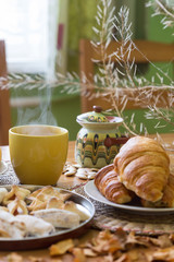 Black tea in yellow mug with croissants, buns and homemade cookies on wooden table