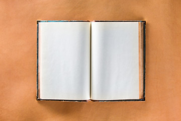 Mockup of opened vintage book with shabby cover and blank pages at brown leather skin background.