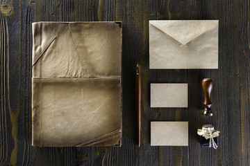 Mockup of vintage stationery set including folio book, business cards and envelope at wooden table background.