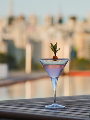 Cocktail glass with rose liquid  on a wooden table against the background of the city