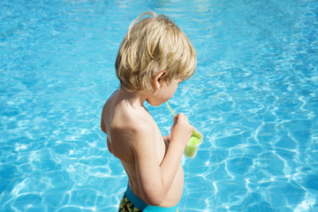 Boy drinks ice from juice at the pool
