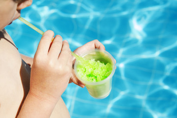 Boy drinks ice from juice at the pool