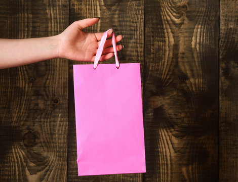pink shopping bag in female hand on wooden background