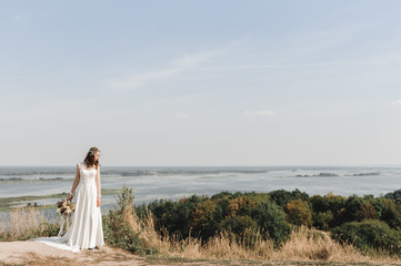 Невеста в свадебном платье на горе с видом на просторный разлив реки