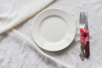 Tableware, white plate, fork, knife on a white tablecloth