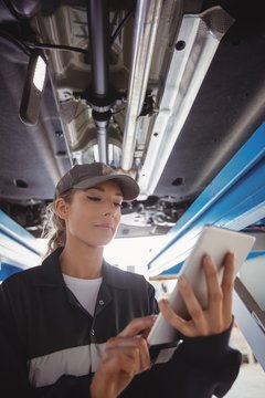Female mechanic using digital tablet under a car