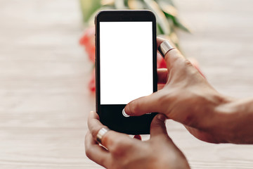 instagram photographer, blogging workshop concept. hand holding phone with empty screen with space for text. pink tulips on white wooden rustic background.