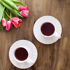 Pink tulips on wooden background, two cups of tea and coffee on saucers with hearts marmalade