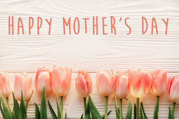 happy mother's day text sign on pink tulips on white rustic wooden background. greeting card...