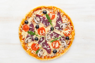 fresh pizza in a rustic Italian style with jerky olives mushrooms and three kinds of cheese on a light wooden background